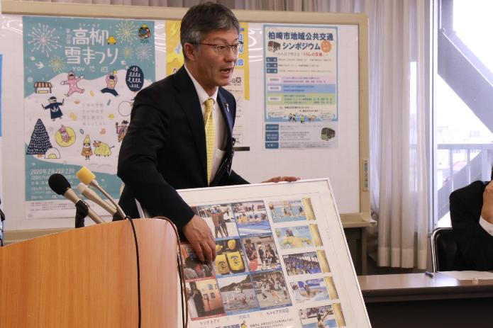 水球関連の写真がたくさん掲載されたパネルを前にフレーム切手発売の説明をする市長