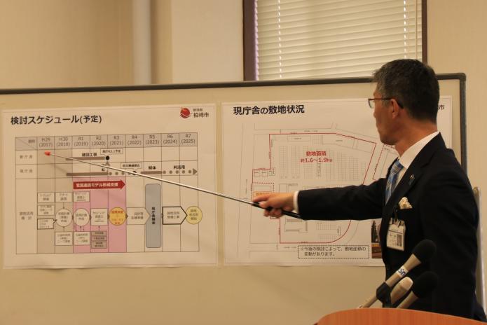 ホワイトボードに貼ってある市役所現庁舎の跡地活用検討資料を差し棒を使って説明する市長の写真