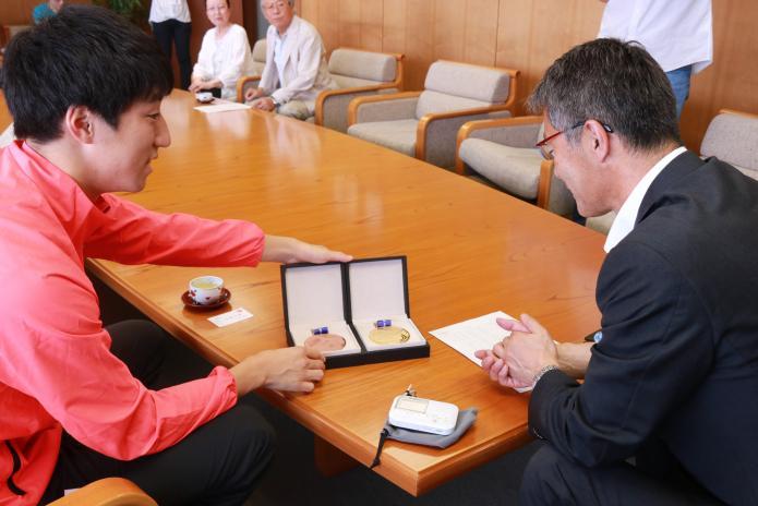 赤いジャージを着た若林選手が、市長に2つのメダルを見せている様子の写真