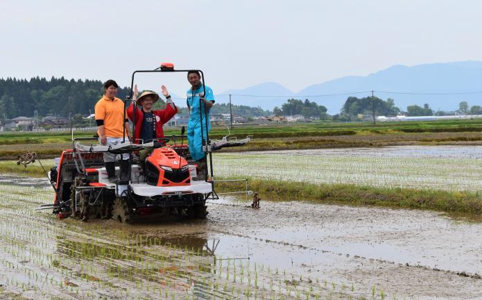 市長が自動運転田植え機にのり万歳をしながら田植えをしている様子の写真