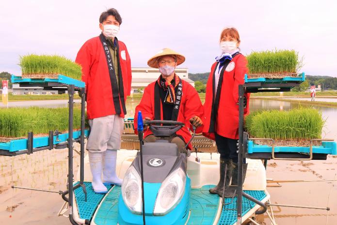 田植機に乗りハンドルを握る市長と、横に立つアグリード越後の加藤さんと小泉さんの写真