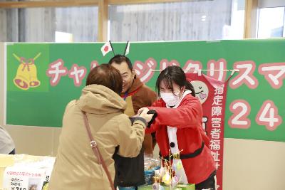 写真：お客さんに笑顔で商品を手渡す女性。サンタクロースの衣装で接客をしています