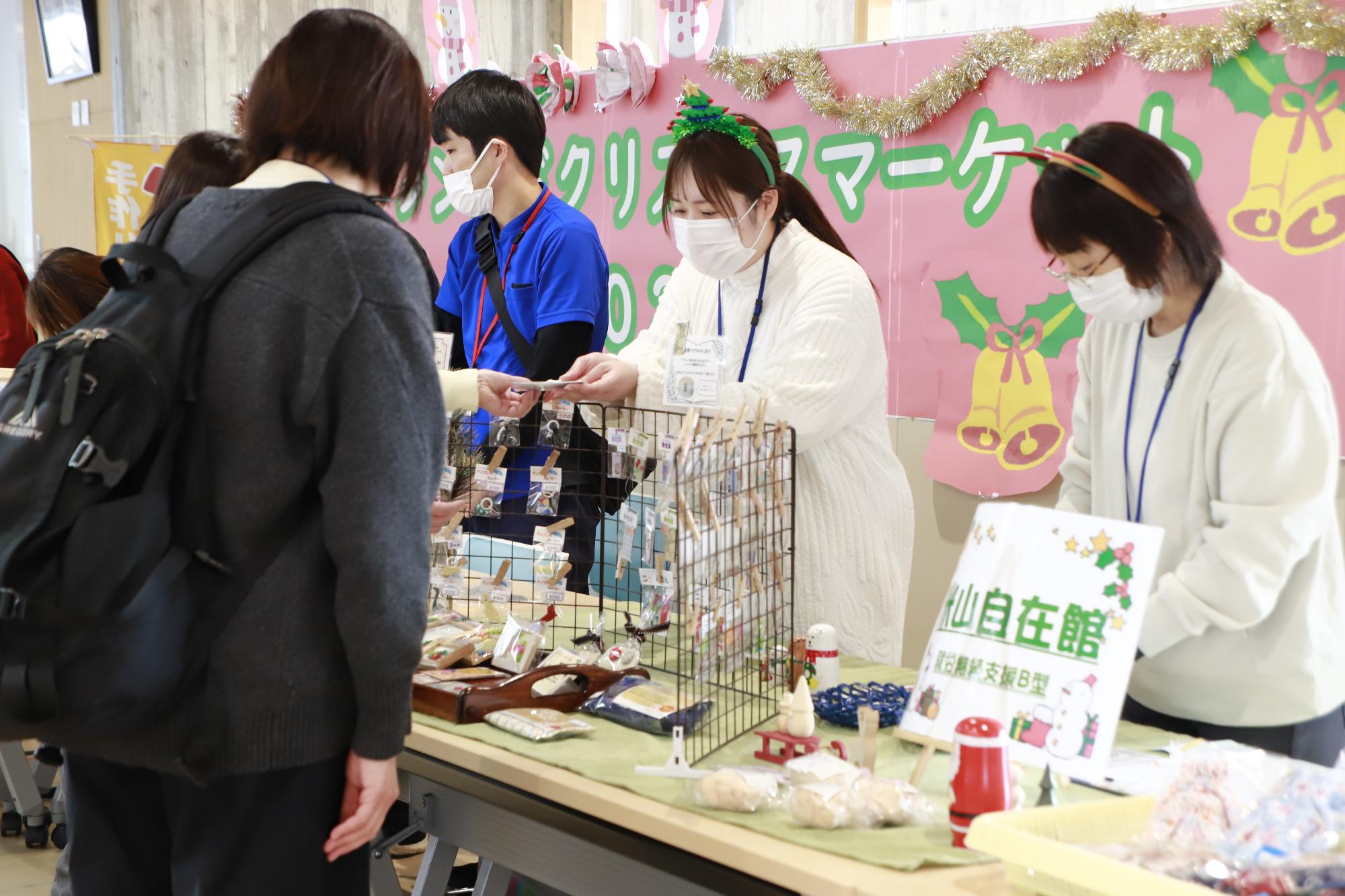 写真：ペーパークラフト・雑貨・加工品を販売する米山自在館の利用者・スタッフ。お客さんに商品を手渡しているところです。（12月23日）