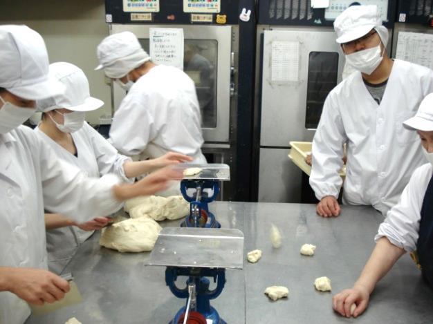 複数の作業員が白衣と帽子を被りパン生地を小分けにしているようすの写真