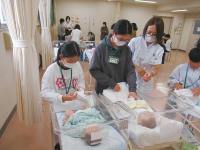写真：赤ちゃんの人形を使ってオムツ交換の体験をする参加児童たち。体験児童には看護士が付き添ってい教えています
