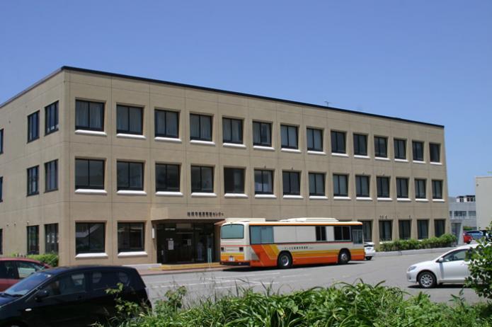 茶色い壁の三階建ての健康管理センターの前にオレンジ色のバスが停まっている写真