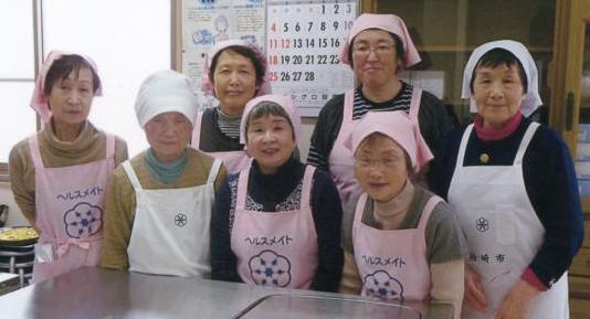 ピンク色や白色のエプロンと三角巾をを身に着けた荒浜地区の食生活改善推進員7名の女性が立っている写真