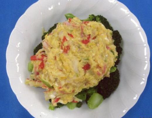 野菜の上ににかにかまぼこが混ざった卵のあんをのせて調理されたブロッコリーのかにあんかけの料理が白い皿の上に盛りつけられている写真