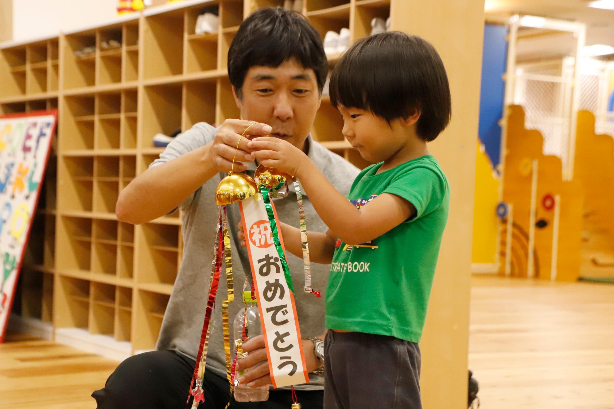 写真：キッズマジック10万人目のお子さんとお父さんがミニくす玉を割ろうとしているところ