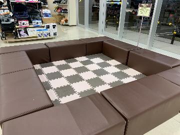 床にクッション材が敷き詰められ、茶色いソファで囲まれたお子様が遊ぶことができるキッズスペース