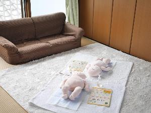 ソファの前にオムツ交換のためのバスタオルが床に敷いてあり、その上に赤ちゃんのお人形があります。