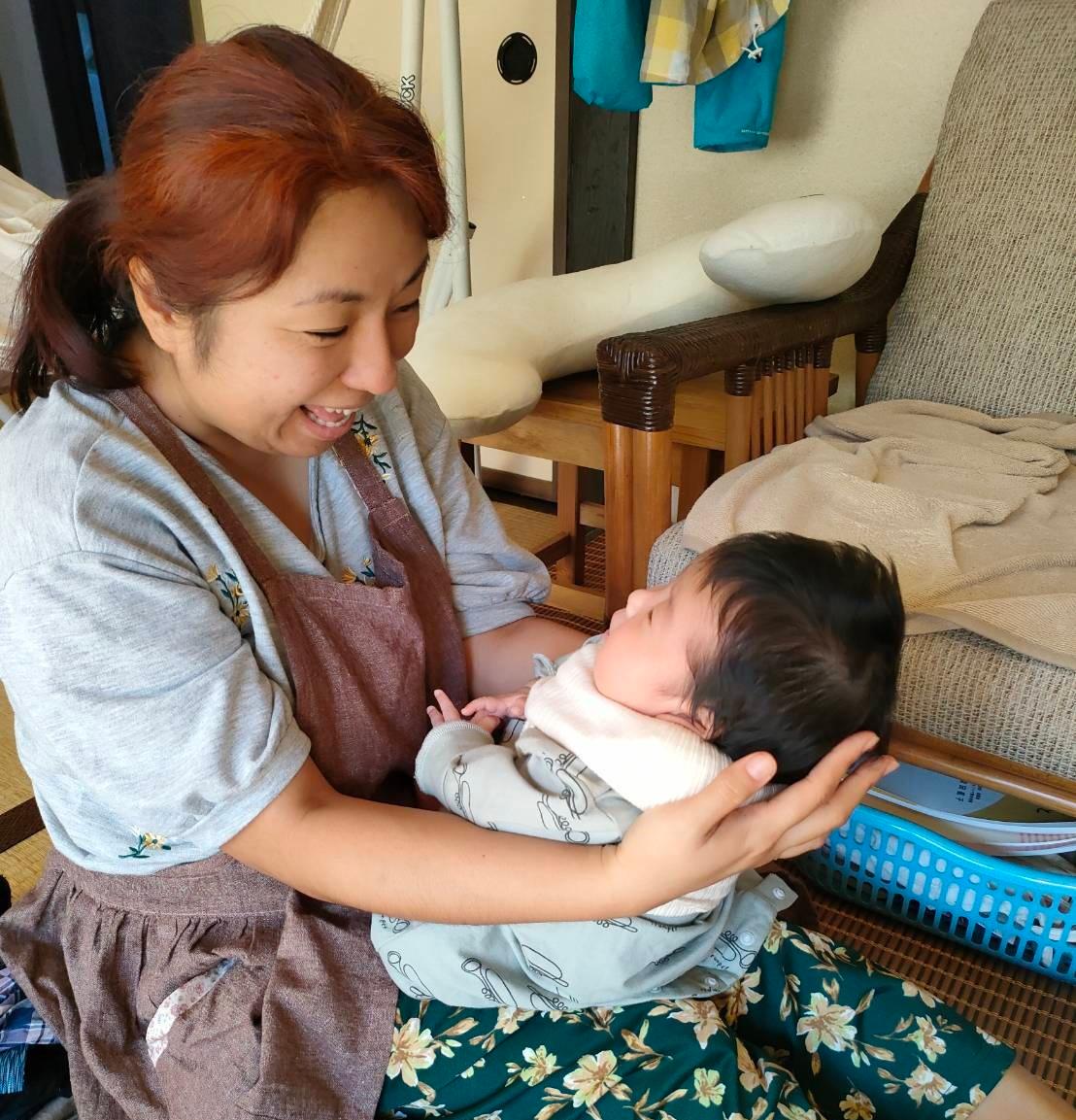 写真：赤ちゃんの顔を見ながら抱っこし、笑顔であやすサービス提供者の女性