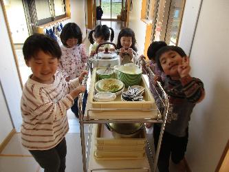 写真：食べ終わった食器や食缶を載せた給食ワゴンを給食室まで運ぶ4歳児