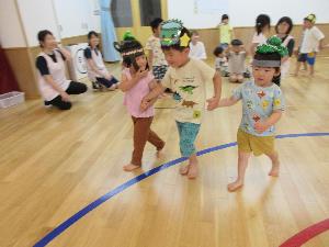 写真：小さいクラスの子どもたちが織姫や彦星の帽子をかぶり大きいクラスのお友達に手を繋いでもらって歩いています。