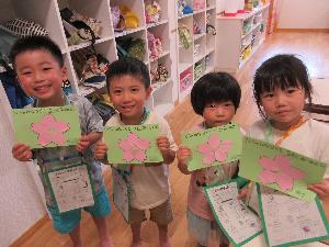 写真：4人の子どもたちが花びらを貼って桜の形を完成させたカードを見せて並んでいます。
