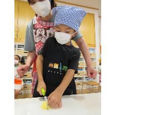 写真：エプロンを身に着けた5歳児が包丁でジャガイモを切っています。