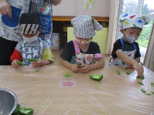 写真：半分に切ったピーマンの種を取り、一口サイズに手でちぎっている3歳児