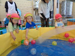 写真：すくい網を使って水風船を取ろうとしている2歳児。横からシャワーのいたずらが入っていました。