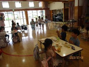 写真：遊戯室に机を集めて、園児全員で食事のあいさつをしています