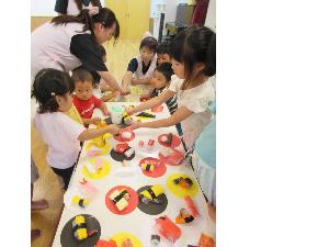 写真：机の上に廃材で制作したお寿司を並べ、子どもたちがお寿司屋さんごっこをしています。