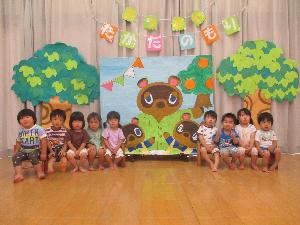 写真：たぬきのキャラクターや2本の木を貼った壁制作の前で、記念写真を撮る未満児