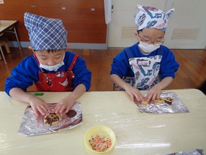 写真：成型した生地の上にチョコなどを使って飾り付けをしている2人の園児