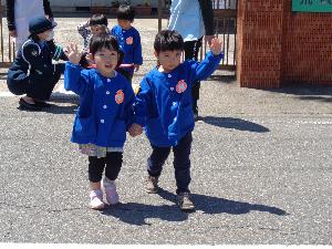 写真：保育園の前で、両手を上にあげて、道路の横断を練習する2人の子どもたち