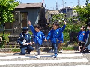 写真：保育園前の横断歩道で、2人組で手をつなぎ、片手を大きく上にあげて道路を渡る練習をする子どもたち