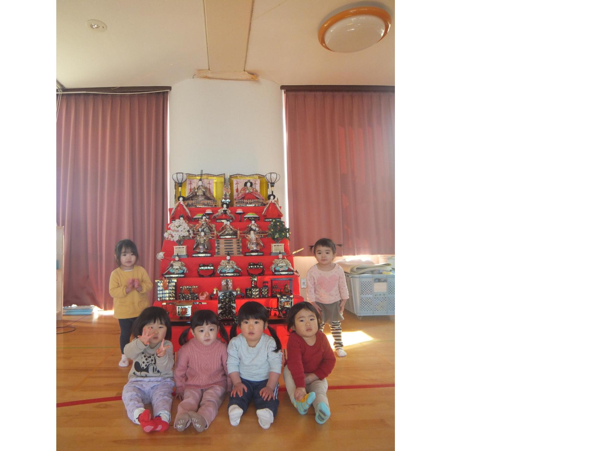 写真：1歳児の子ども達6人が、雛飾りの前で写真を撮っている様子