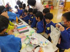 写真：机に並んだ手作りおもちゃの前には、たくさん子どもたちで人だかりができています。