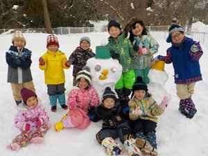 写真：3歳以上児10人が自分たちで作った雪だるまの周りに集まり、ポーズをとっているところ