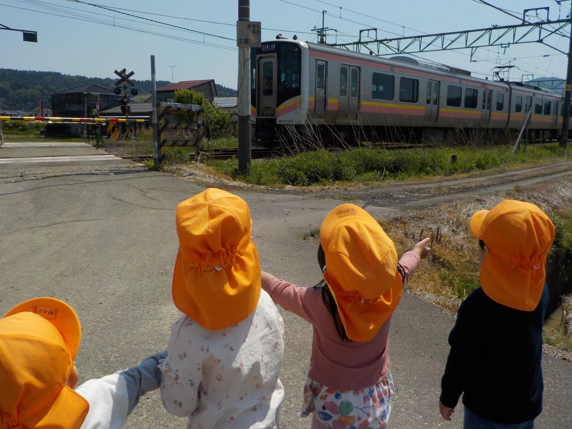 写真：4人の子どもが踏切の前で、通り過ぎる電車に手を振っているところ