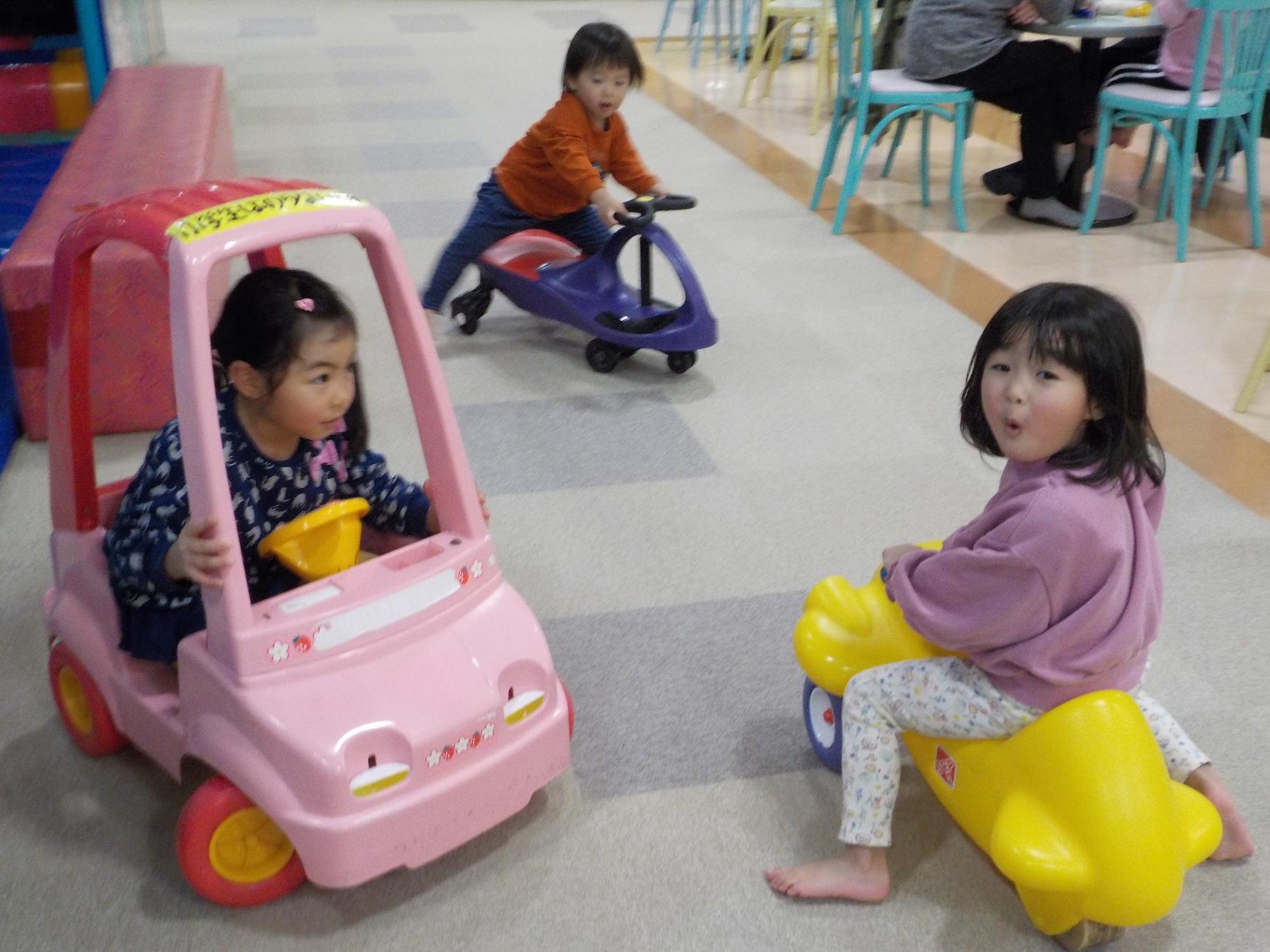 乗り物の遊具に乗り、遊ぶ2人の女の子の後ろで、乗り物の遊具に乗ろうとする男の子