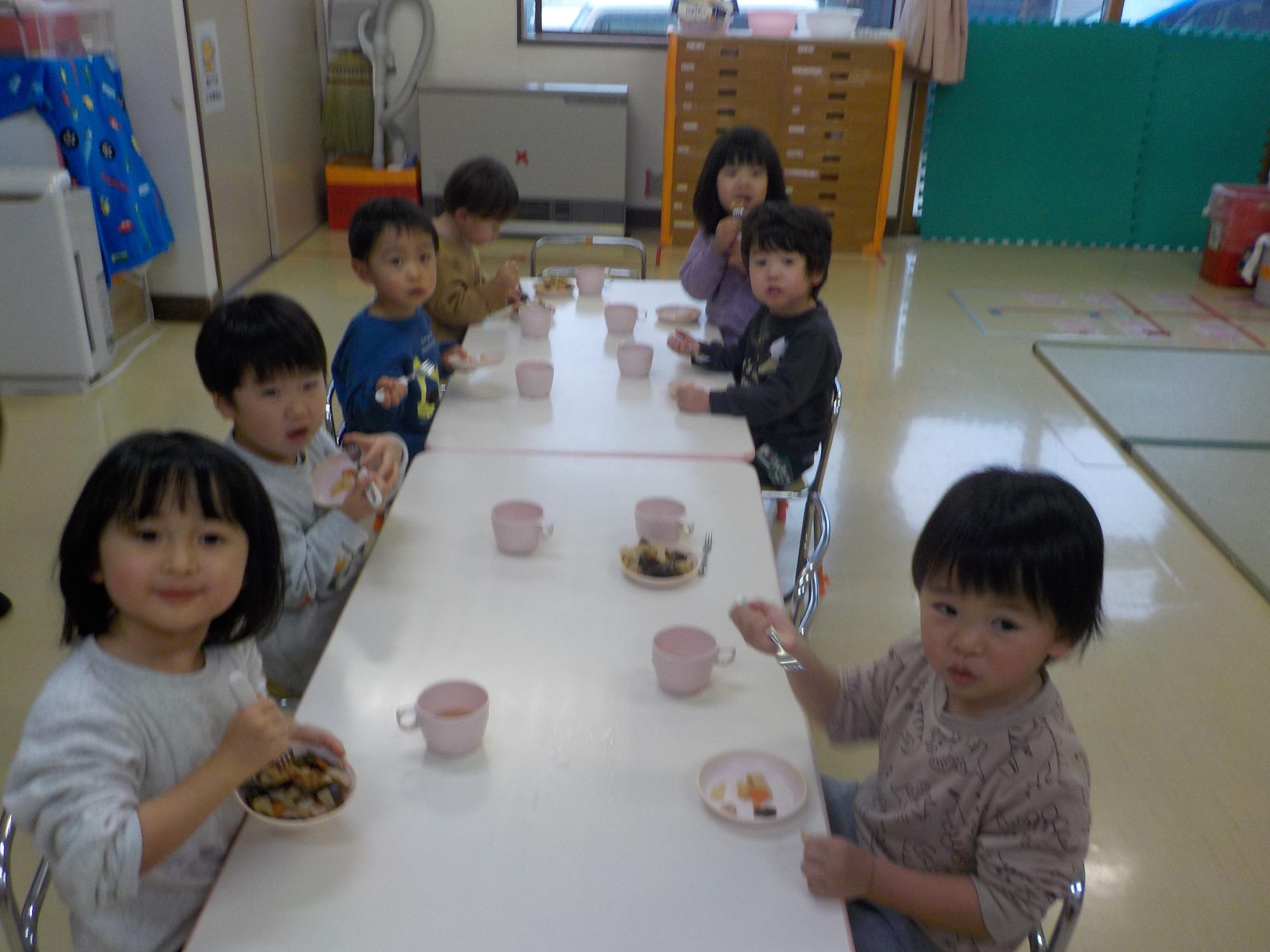 テーブルに向かい、椅子に座っておやつのおでんを食べているうさぎ組の子どもたち