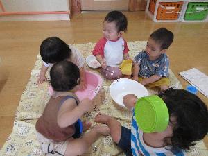 写真：室内に敷いたシートの上で、ボールに入った氷や温水を触って遊ぶ0～1歳児の子どもたち