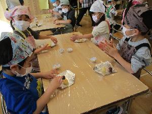 写真：年長児4名がクッキー生地を手で丸めたり伸ばしたりしています。