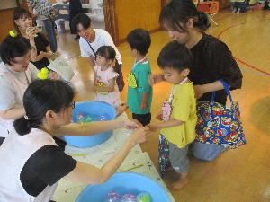 写真：子どもが親子でヨーヨー釣りをしている様子。保育士が釣った水ヨーヨーを子どもの手にかけているところ