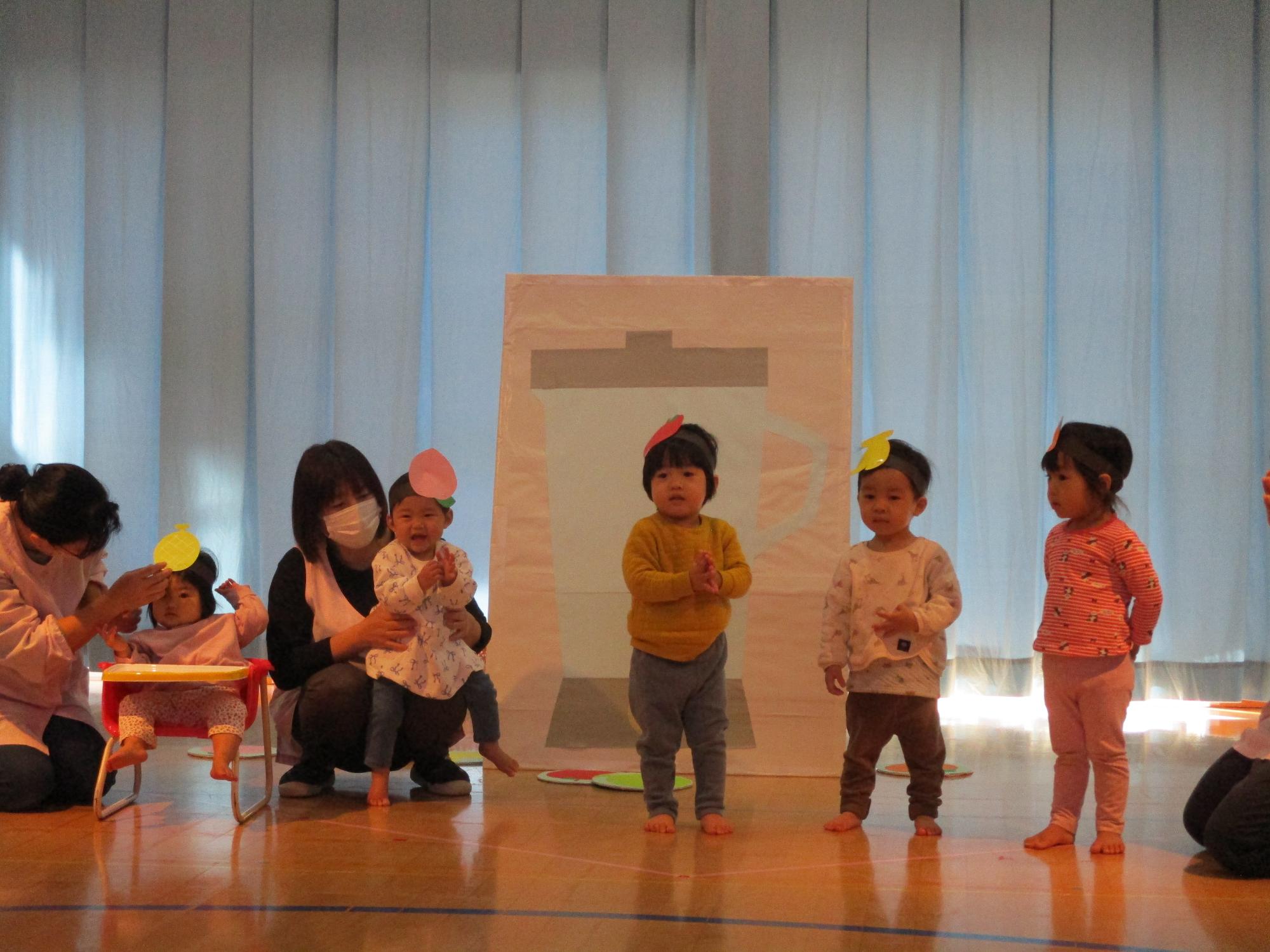 写真：果物のお面をつけ、ミックスジュースの歌に合わせて手遊びを披露するしひよこ組の子どもたち