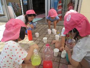 写真：ペットボトルに入れた赤と黄色の色水をカップに入れ替えて、色の変化を楽しむ子どもたち