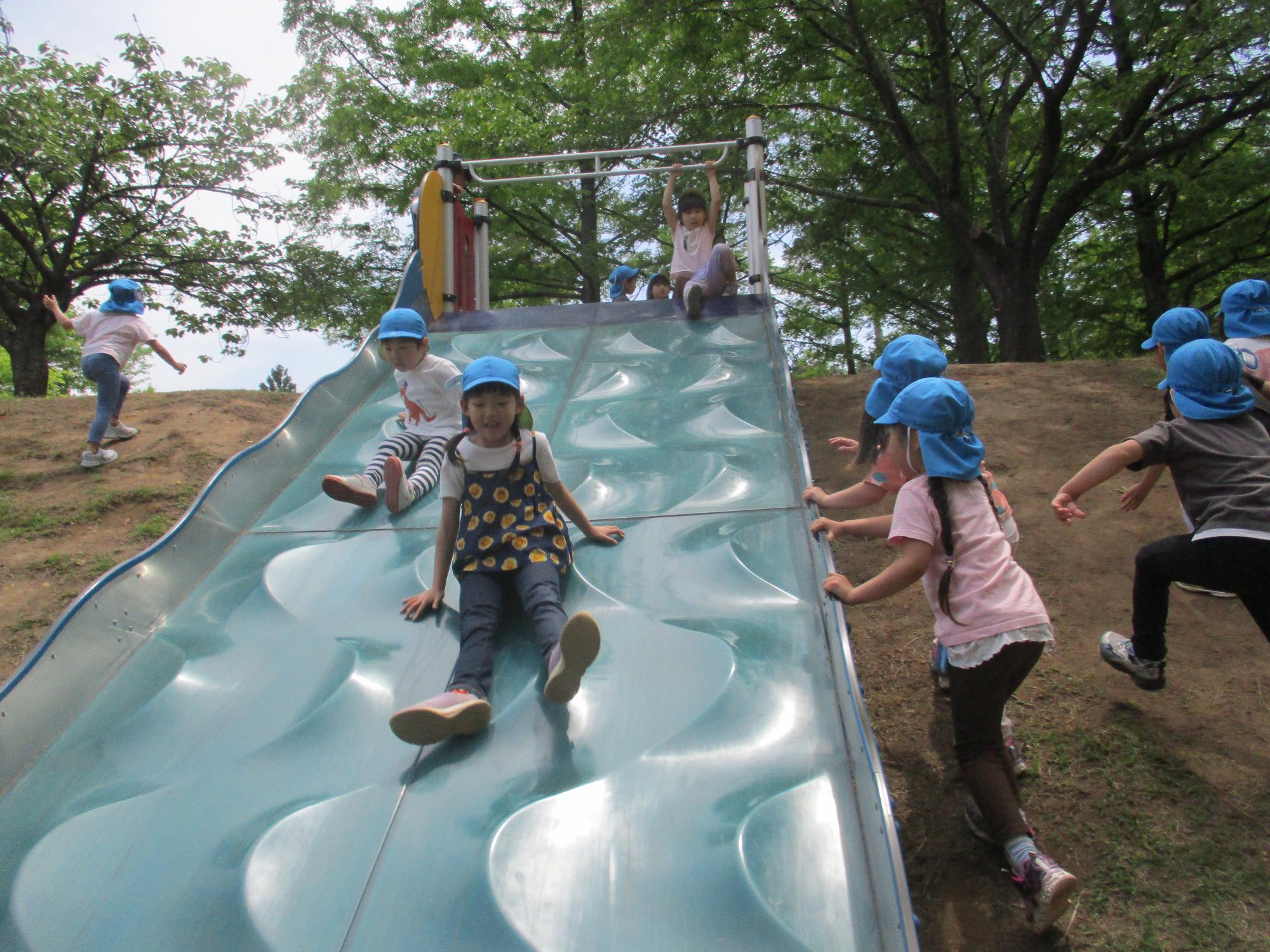 写真：子どもが3人並んでも余裕のある幅の大きなすべり台を滑る2人の園児。滑る面になだらかなでこぼこ模様をしています。