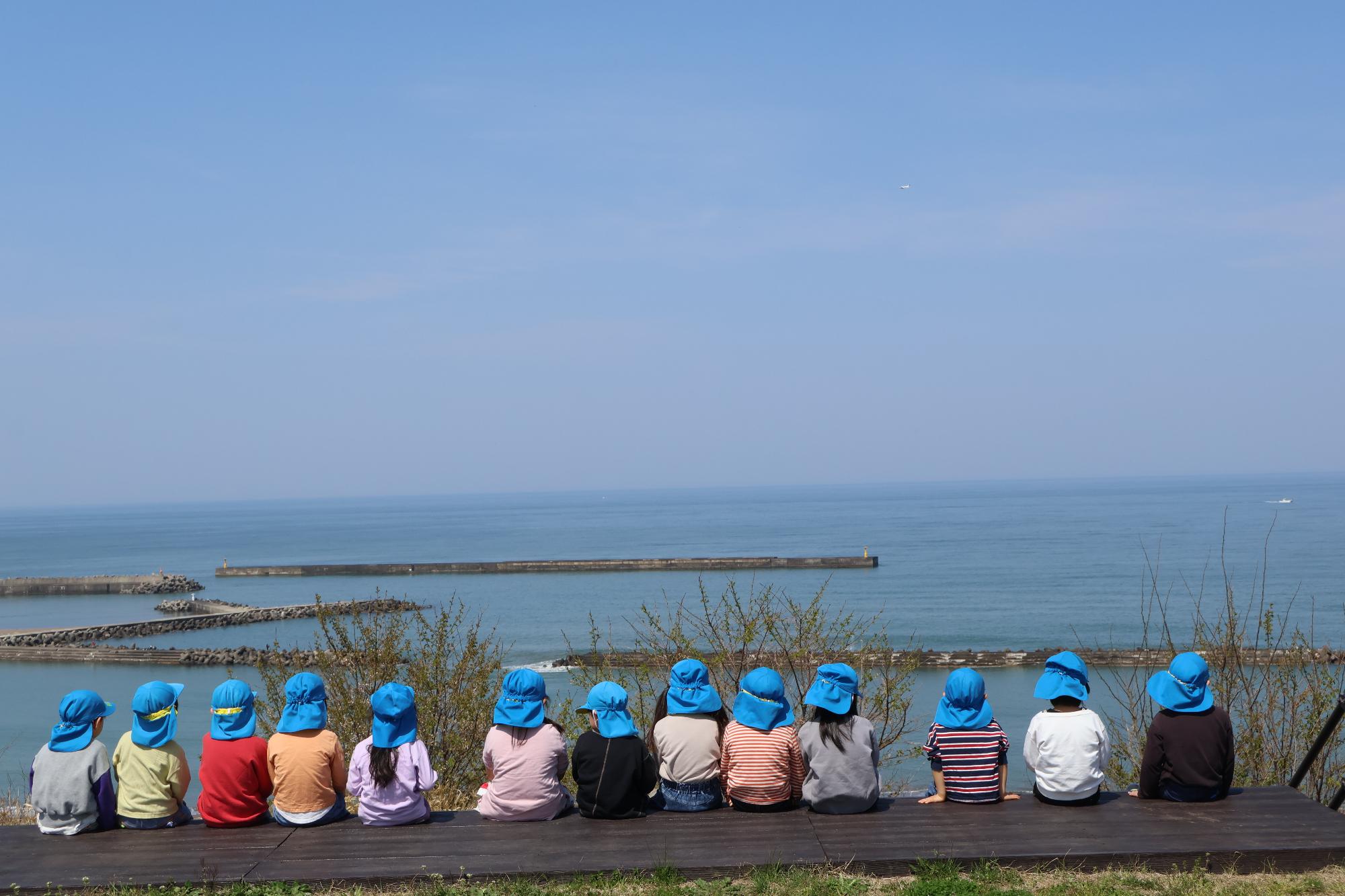 写真：日本海が一望できる夕日の森公園のベンチに子ども達が一列に座り、海を眺めています