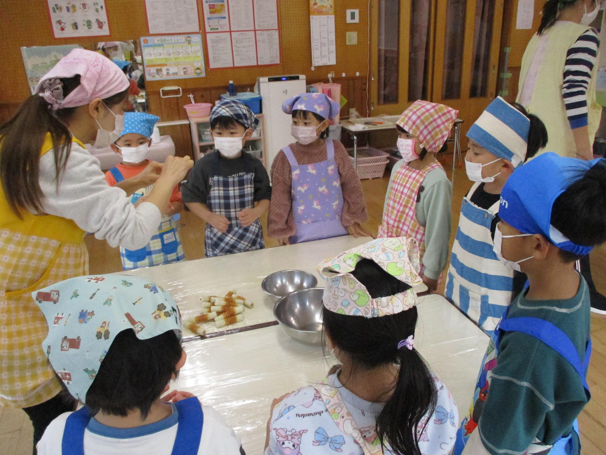 写真：先生がちくわをちぎる様子を真剣な表情で見ている4歳児の子どもたち