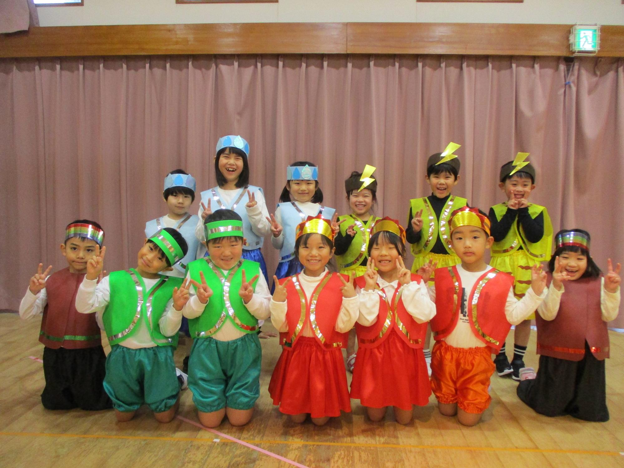 写真：役柄ごとに緑・黄・オレンジ・茶・水色の衣装を着たきりん組の子どもたち