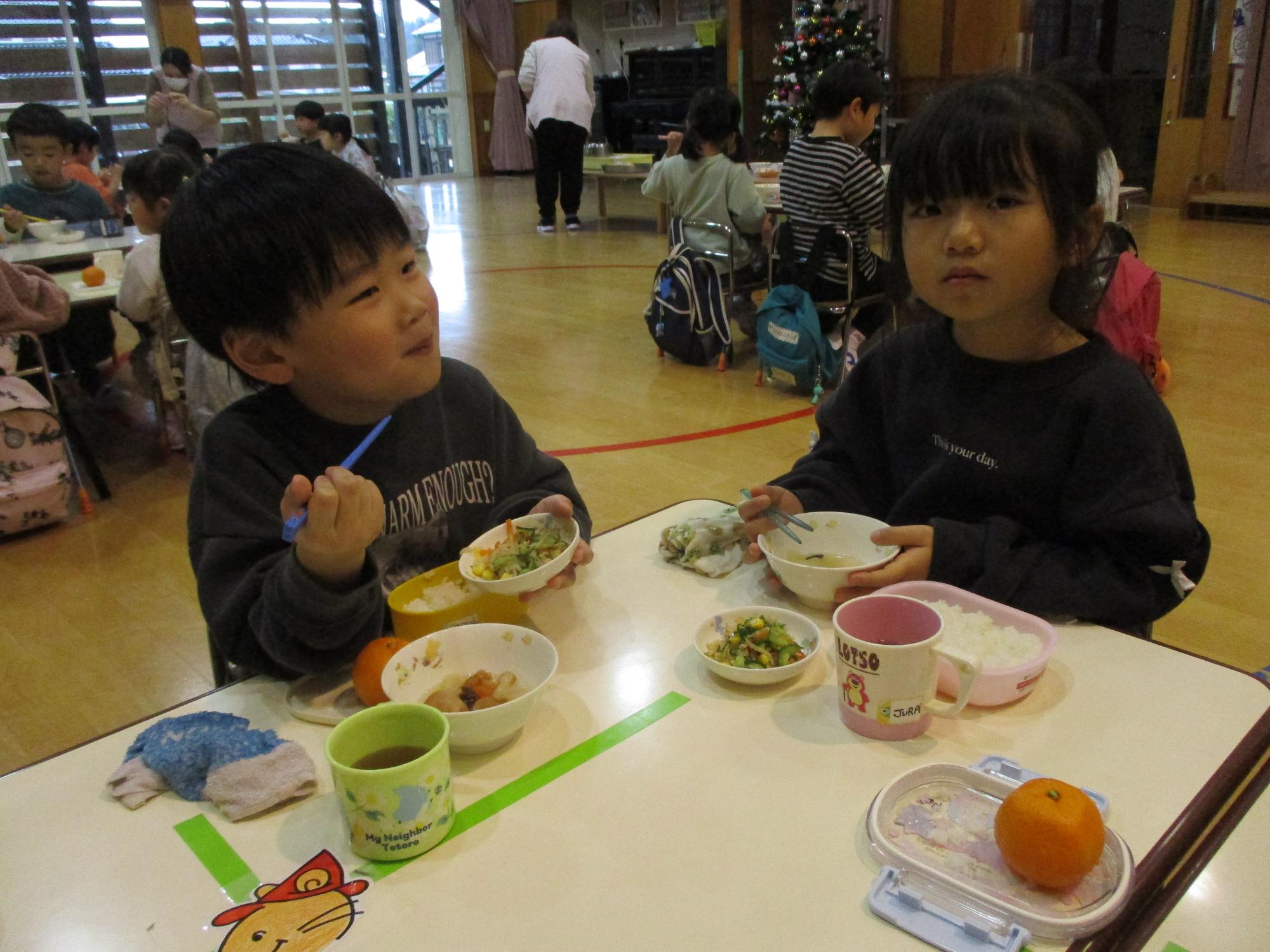 写真：お遊戯室でいくつかのグループに分かれ、できあがったおでんで会食する子どもたち。どの子もおいしそうな表情をしています。