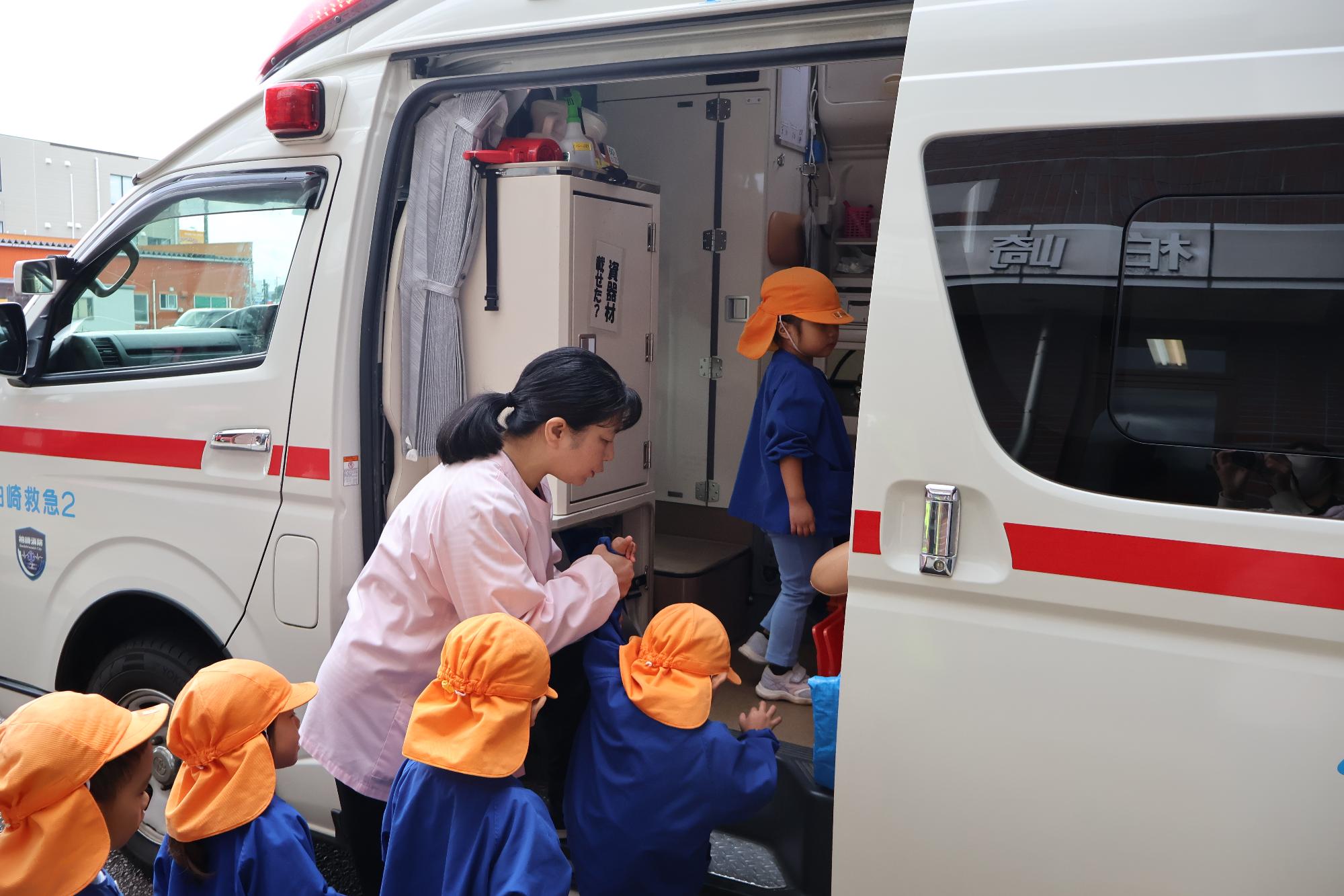写真：列になって、順番に救急車の中に入っていく子どもたちと手を添える先生