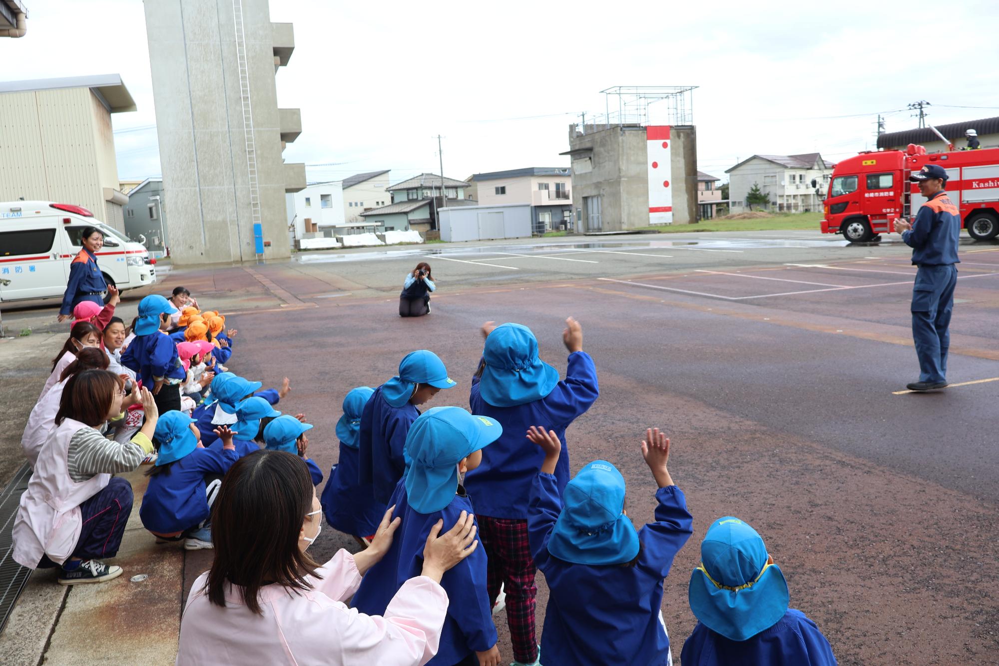 写真：消防車で放水してくれた消防士に手を振る子どもたちと先生