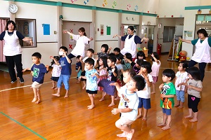 写真：子どもたちと保育士が両手を横に広げ片足立ちのポーズをしています。
