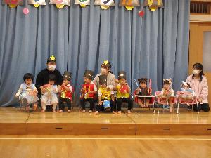 写真：発表会のリハーサルの様子。おもちゃに扮した衣装を着て、上手に座っている子どもたち。