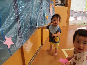 写真：水色のカラーポリシートで作った天の川に、星型の画用紙を張り付ける一歳児の子どもたち