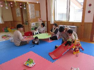 写真：滑り台などの好きなおもちゃで遊ぶ親子、保育士と話をしている親子がいます。